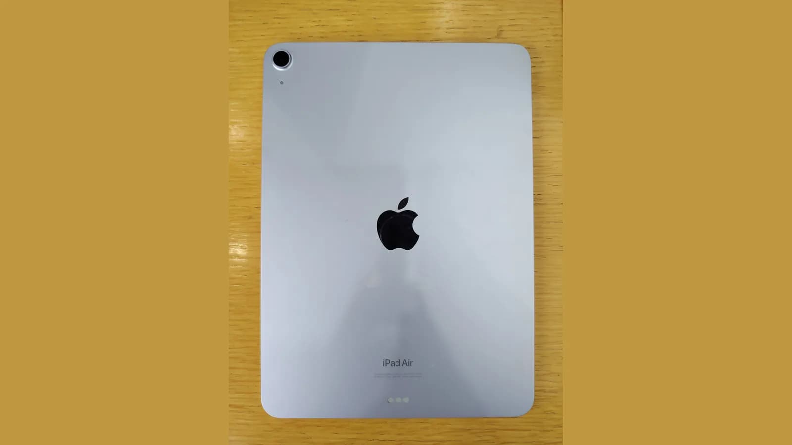 Bahagian belakang biru muda sebuah iPad di atas meja kayu, dengan logo Apple di tengah, kamera di satu sudut dan perkataan iPad Air tercetak berhampiran bahagian bawah