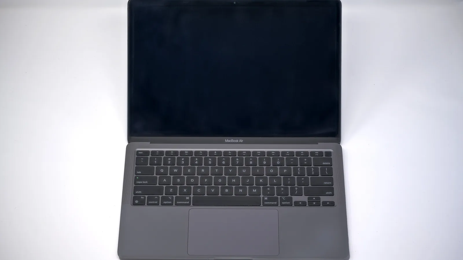 An open space-grey MacBook Air seen from above on a plain white surface, its screen switched off and dark, with the black keyboard, the wide trackpad and the name 'MacBook Air' under the screen
