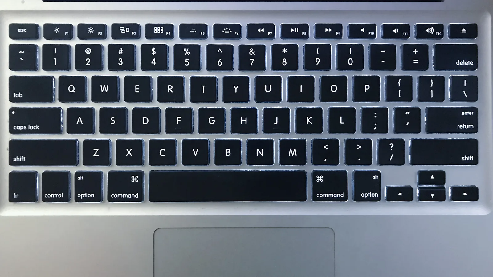 Gambar dekat papan kekunci MacBook Pro berlampu latar dengan kekunci susun atur AS bersinar dalam gelap.