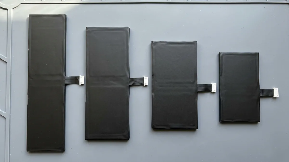 Four blank black laptop battery packs of different lengths and thicknesses laid out in a row and seen from above, each with a short ribbon tail pointing the same way.