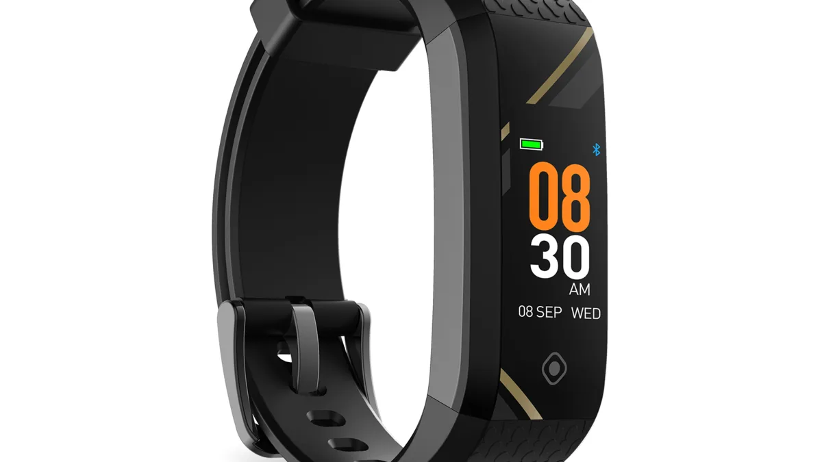 An Actxa Spark fitness band with a black strap and a gold accent stripe, its colour screen lit, standing on a plain white background