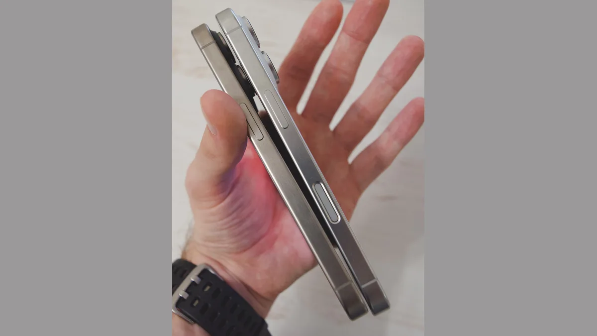 一只手托着两部侧立的 iPhone，可以看到拉丝钛金属边框和侧边按键，两块屏幕都朝向另一侧