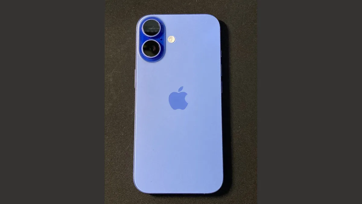一部蓝色 iPhone 背面朝上平放在深色布面上，可以看到竖排双镜头、闪光灯和苹果标志