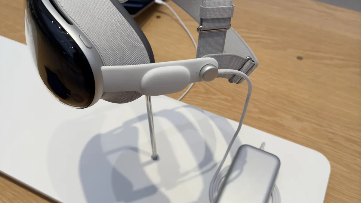 An Apple Vision Pro on a retail display stand with its external battery pack beside it