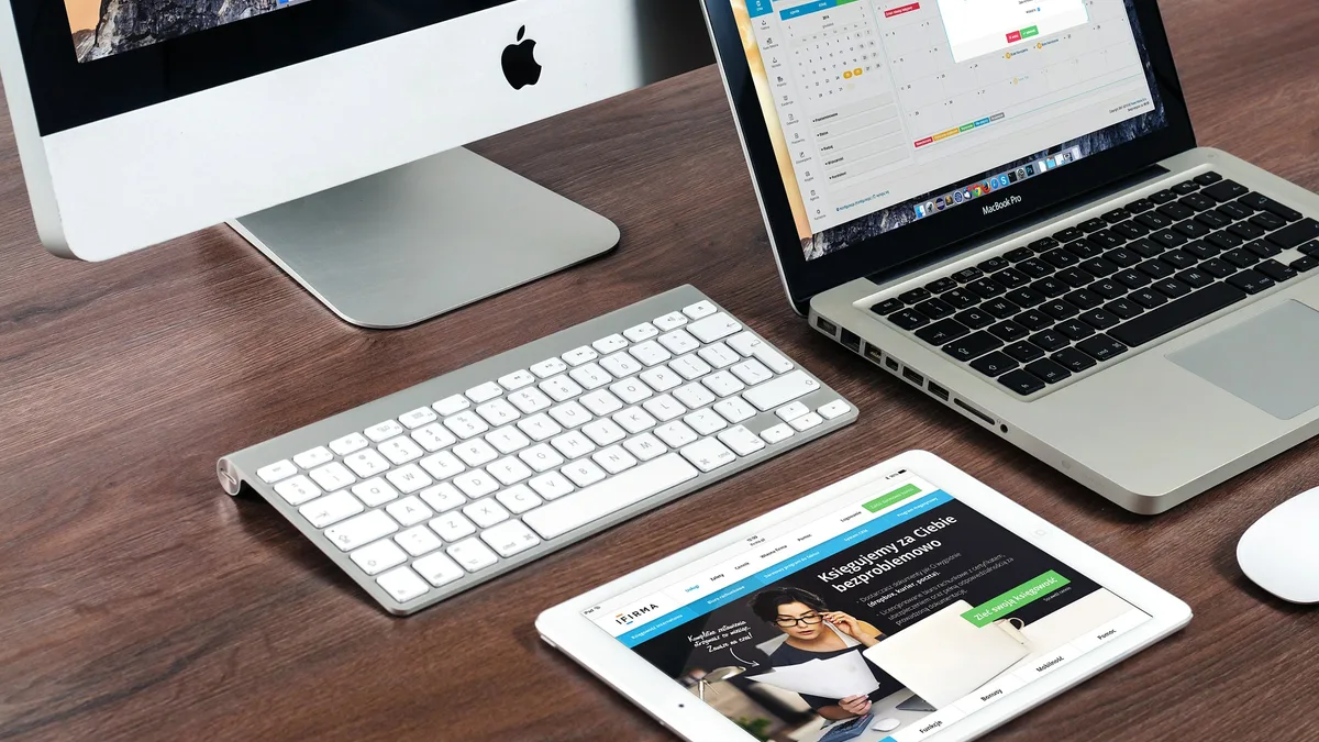 Sebuah iMac, MacBook dan iPad di atas satu meja dengan papan kekunci tanpa wayar