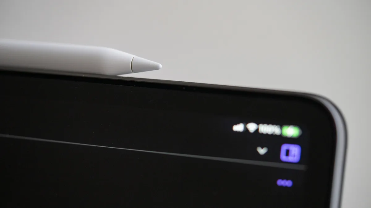Sebatang Apple Pencil terletak di tepi iPad Pro, dengan ikon status menyala di bahagian atas skrin