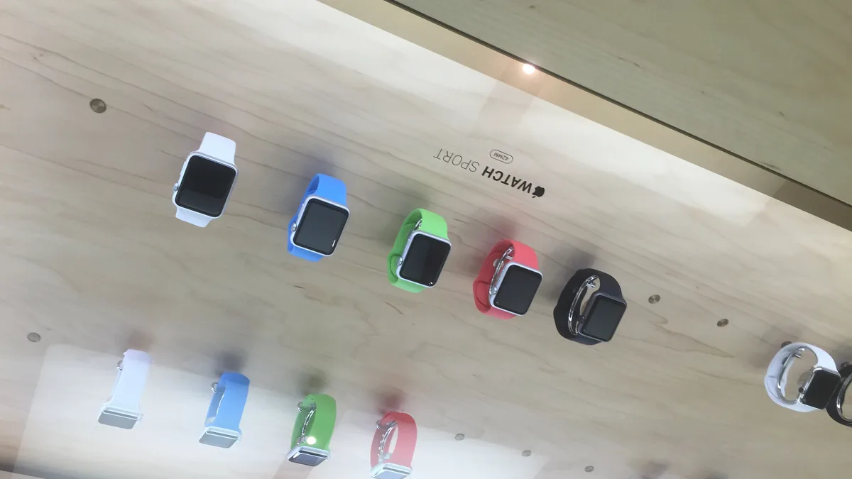 Sederet Apple Watch dengan tali pelbagai warna disusun di atas meja pameran kayu berwarna cerah