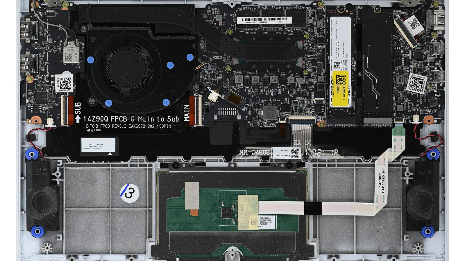 A laptop with its bottom cover removed, seen from above: a black circuit board across the top with a round cooling fan under a black cover marked by blue dots, a long module with a yellow and white label on the right, and a black ribbon cable printed 'Main to Sub'; below it, empty grey compartments, a green touchpad board with a white ribbon cable, and a black speaker in each bottom corner