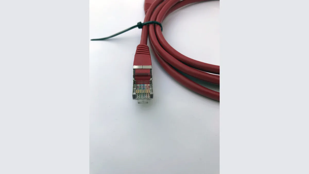 Kabel rangkaian RJ45 merah yang digulung di atas permukaan pucat, penyambung jernihnya menghadap kamera dengan lapan sesentuh emas dan pasangan berpintal kelihatan di dalam