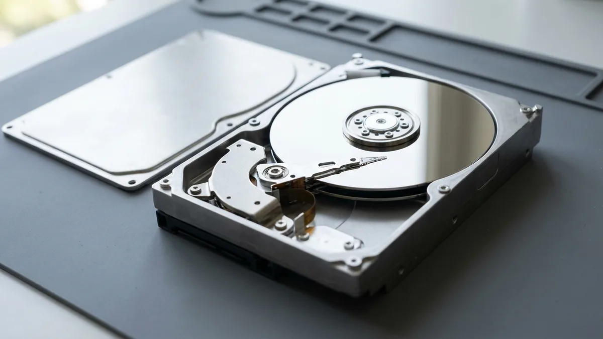 A 3.5-inch desktop hard disk with its top cover removed and set aside, showing the mirror-finish platter, the spindle hub and the slender head actuator arm swung across the disc.