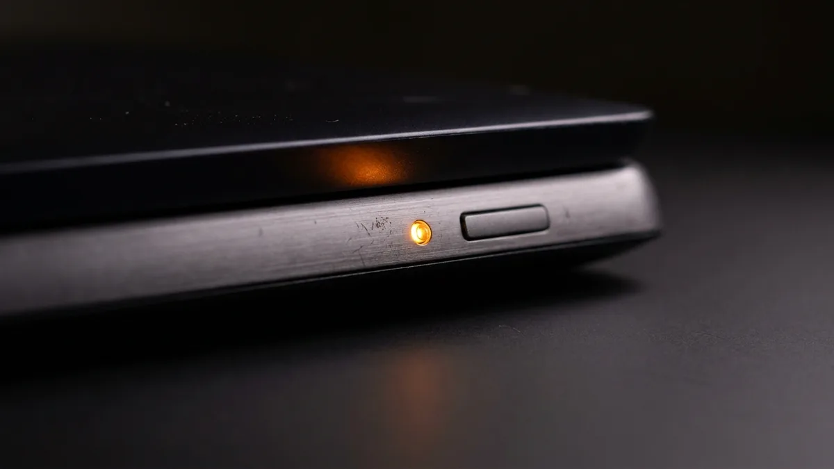Amber status light glowing beside the power button on a closed, unbranded laptop in a darkened room