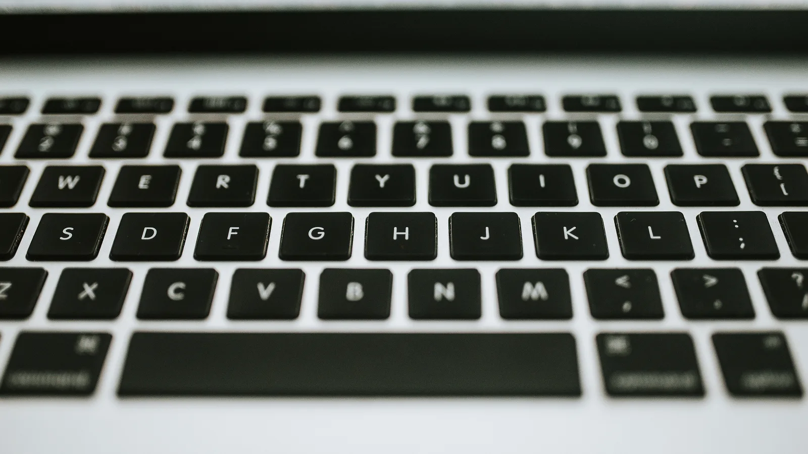 Gambar dekat papan kekunci MacBook, kekunci hitam individu fokus tajam pada top case perak.