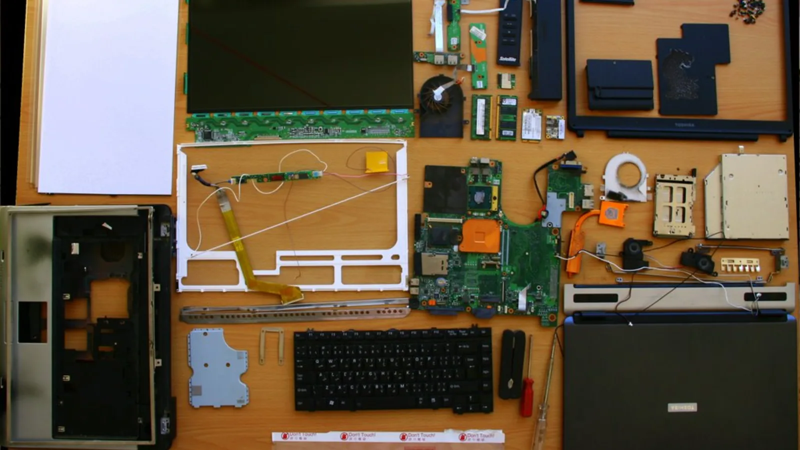 Sebuah laptop Toshiba yang dibuka sepenuhnya, papan induk, pemacu dan lapisan skrinnya disusun di atas permukaan.