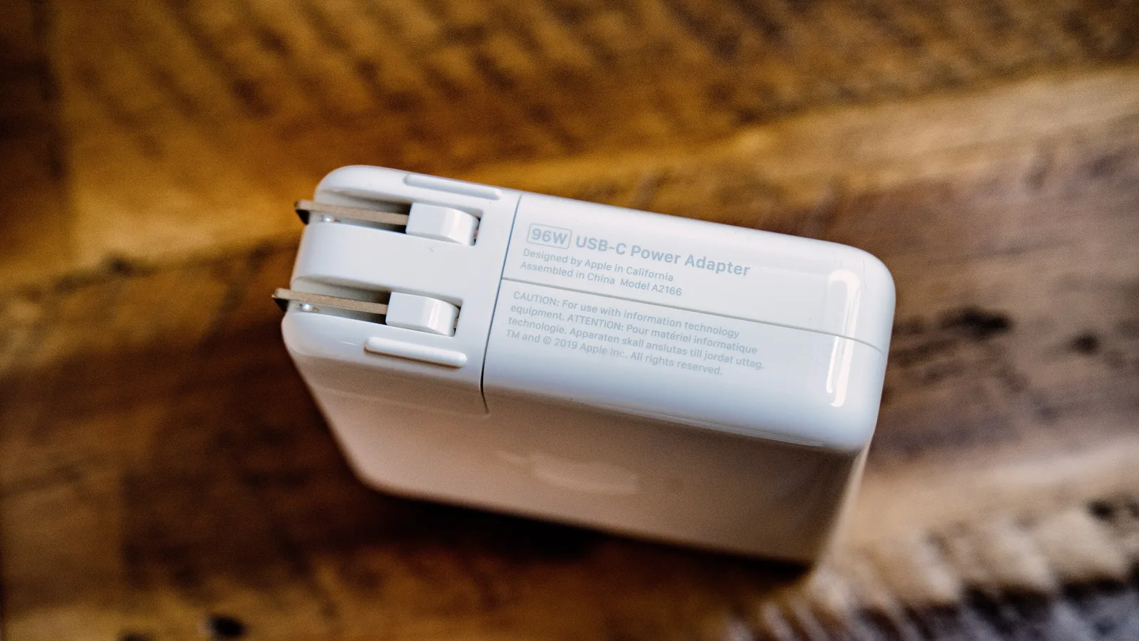 一个白色 Apple 96W USB-C 电源适配器，带可折叠插脚，放在木质桌面上
