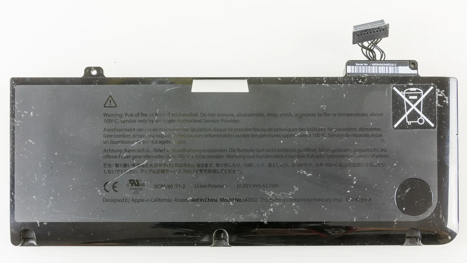 从上方拍摄的黑色长方形 MacBook Pro 锂离子电池，上面印有安全警告和认证标志，顶部有排线接头