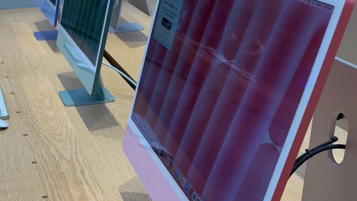 Three 24-inch iMacs in different colours - pink in the foreground, then green and blue - standing in a row on a light wooden table