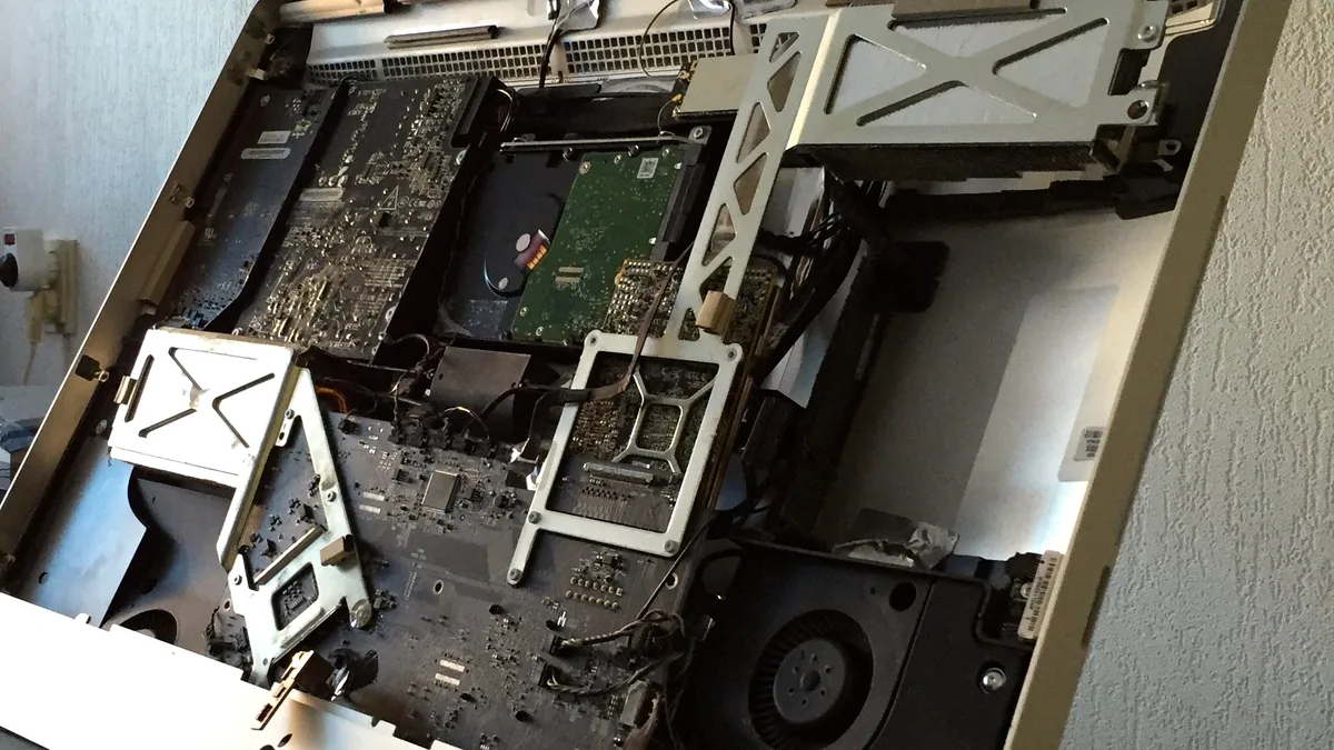The inside of an iMac with its display panel removed, the hard drive, logic board, cooling fan and mounting brackets packed against the back of the chassis