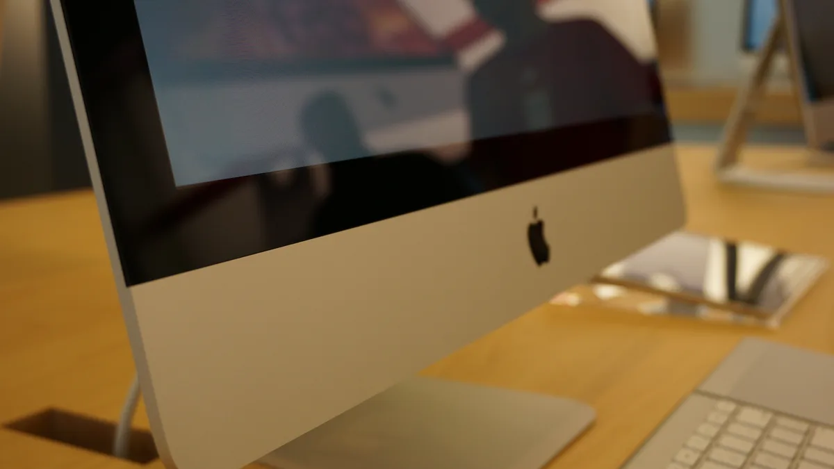A close, low-angle view along the edge of a slim aluminium iMac, the dark glass panel sitting flush against the chassis as it tapers away