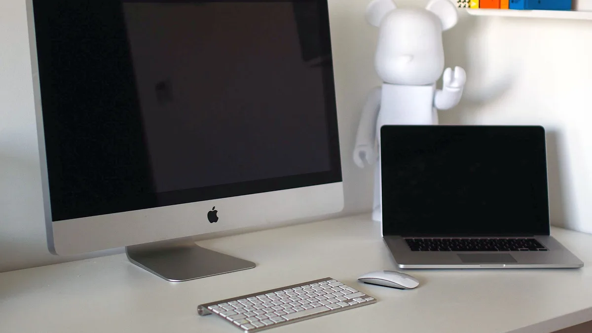 An aluminium iMac back in place on a clean white desk beside a MacBook, its screen dark, with a wireless keyboard and mouse in front
