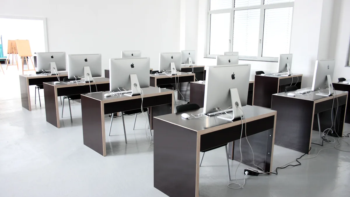 A bright, empty studio room with a dozen aluminium iMacs set out on dark desks in rows, every screen switched off