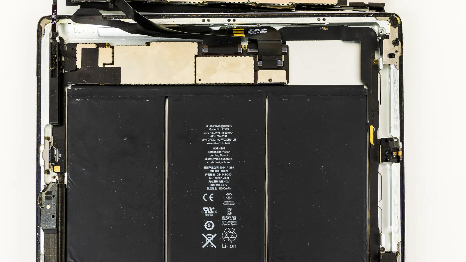 An opened iPad with the display removed, a large black lithium-polymer battery of three flat cells filling the lower half, its white label reading 'Li-ion Polymer Battery' with warning and recycling marks, and a metal-shielded circuit board with ribbon cables across the top