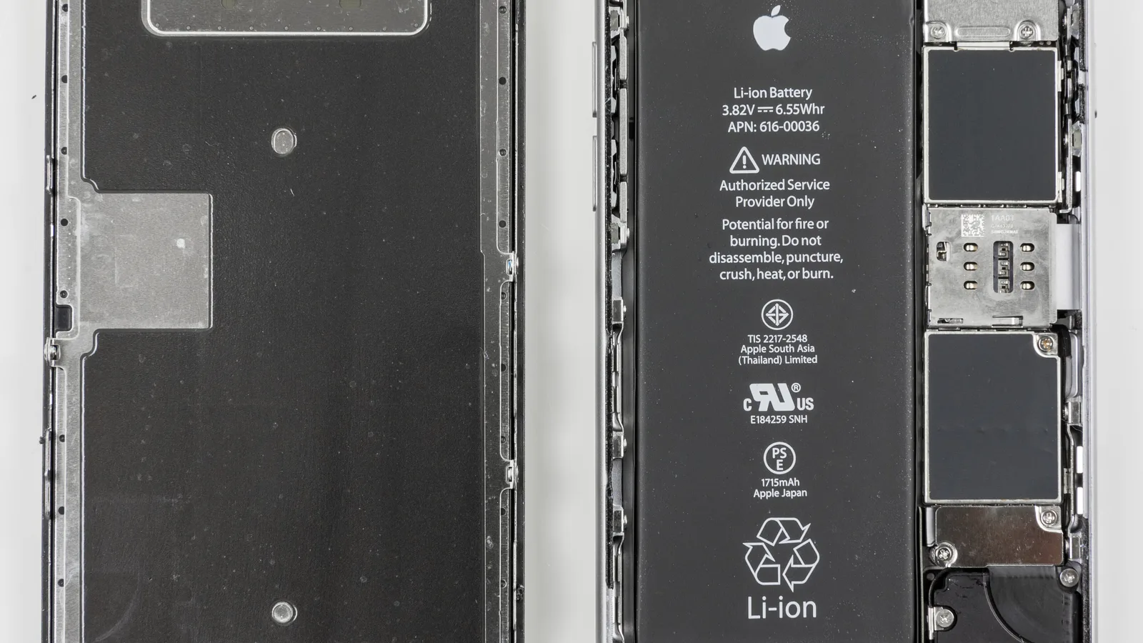 An opened iPhone on a white surface, its two halves side by side: on the left the dark metal back of its screen, on the right a black Apple lithium-ion battery printed with safety warnings, and the circuit board under metal covers along the right edge