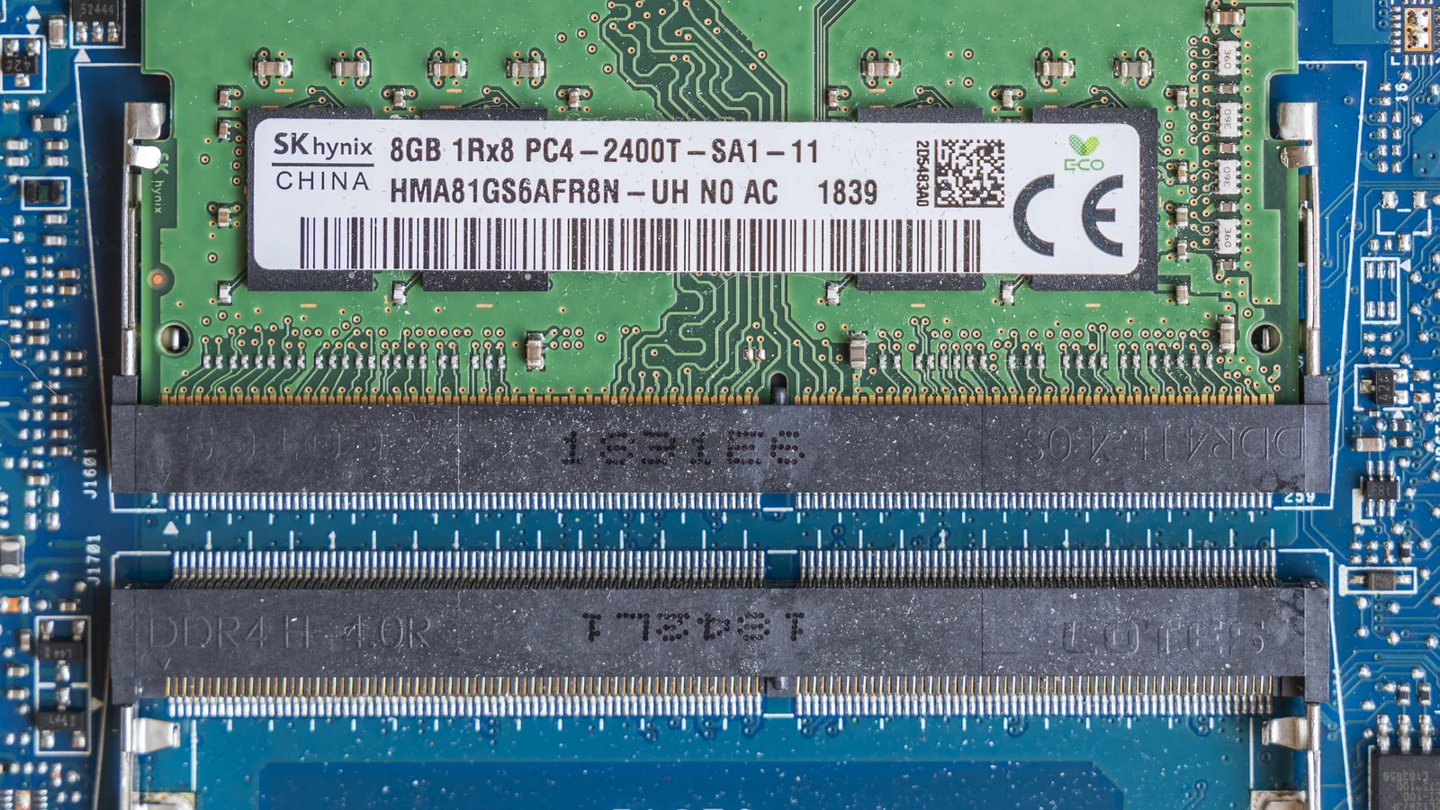 Gambar dekat papan litar komputer riba: modul memori SK hynix 8GB dipasang di slot atas, dan slot memori kosong di bawahnya