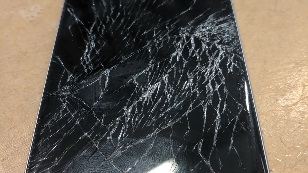 A badly cracked iPhone screen on a workbench — the repair this whole decision is about