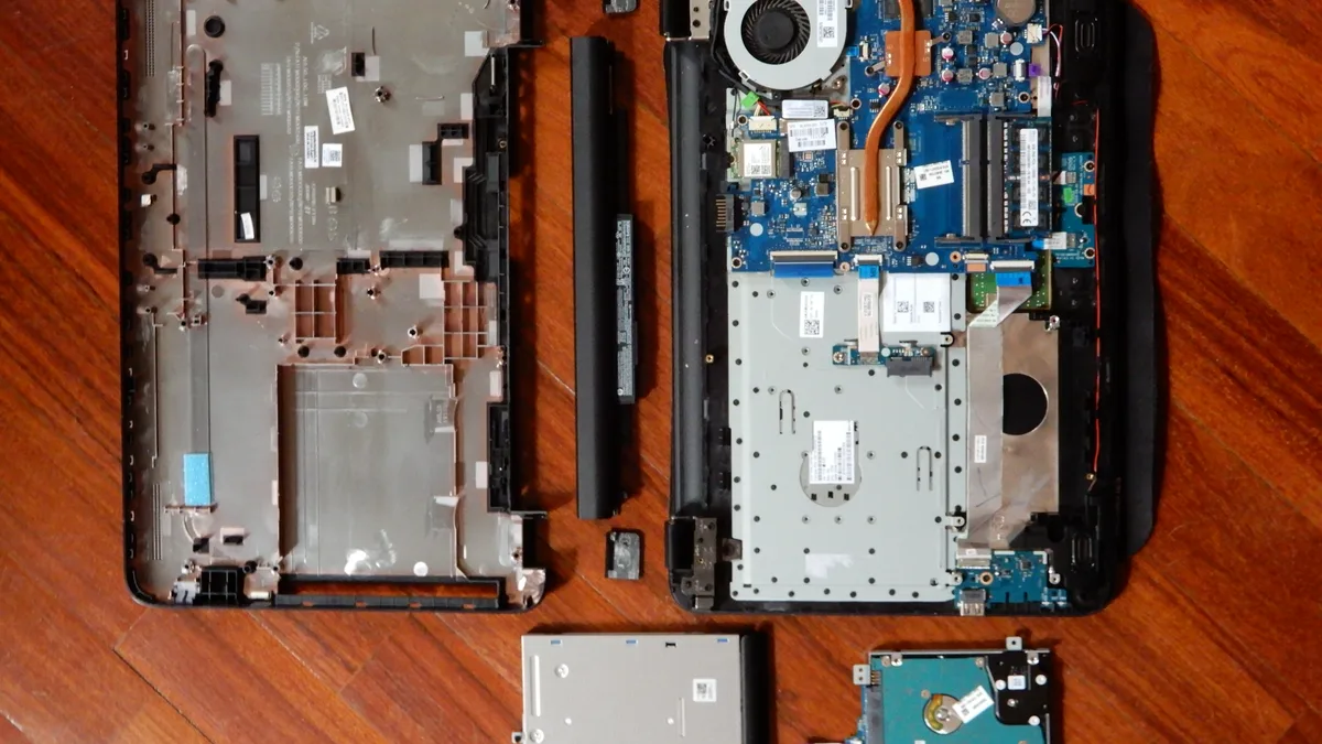 A laptop with its base cover and battery removed, showing the mainboard, cooling fan and drive bay inside