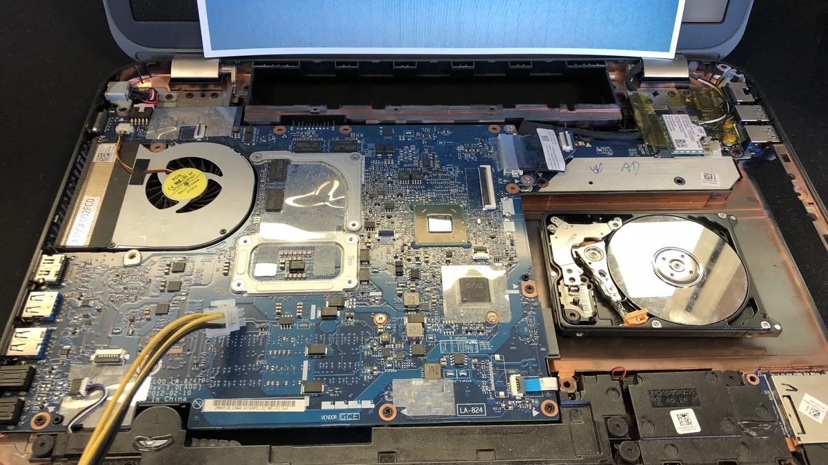 A laptop opened down to the mainboard, with the cooling fan, the processor and a mechanical hard disk exposed beside it