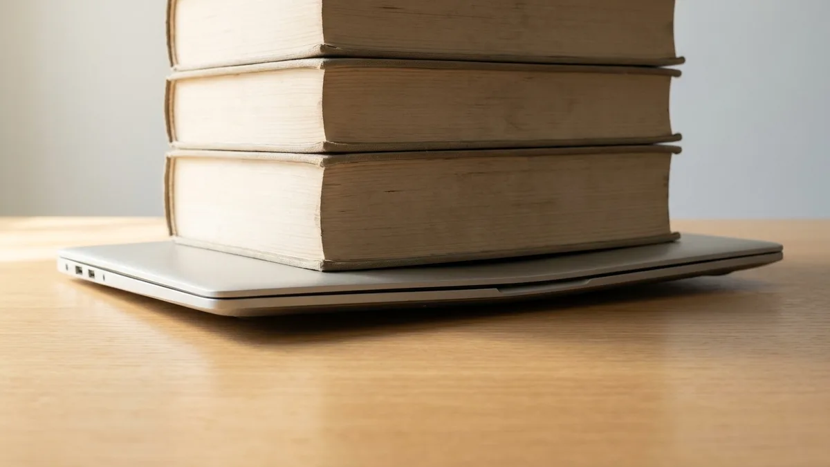 A stack of heavy books resting on a closed laptop lid, bowing it under the weight