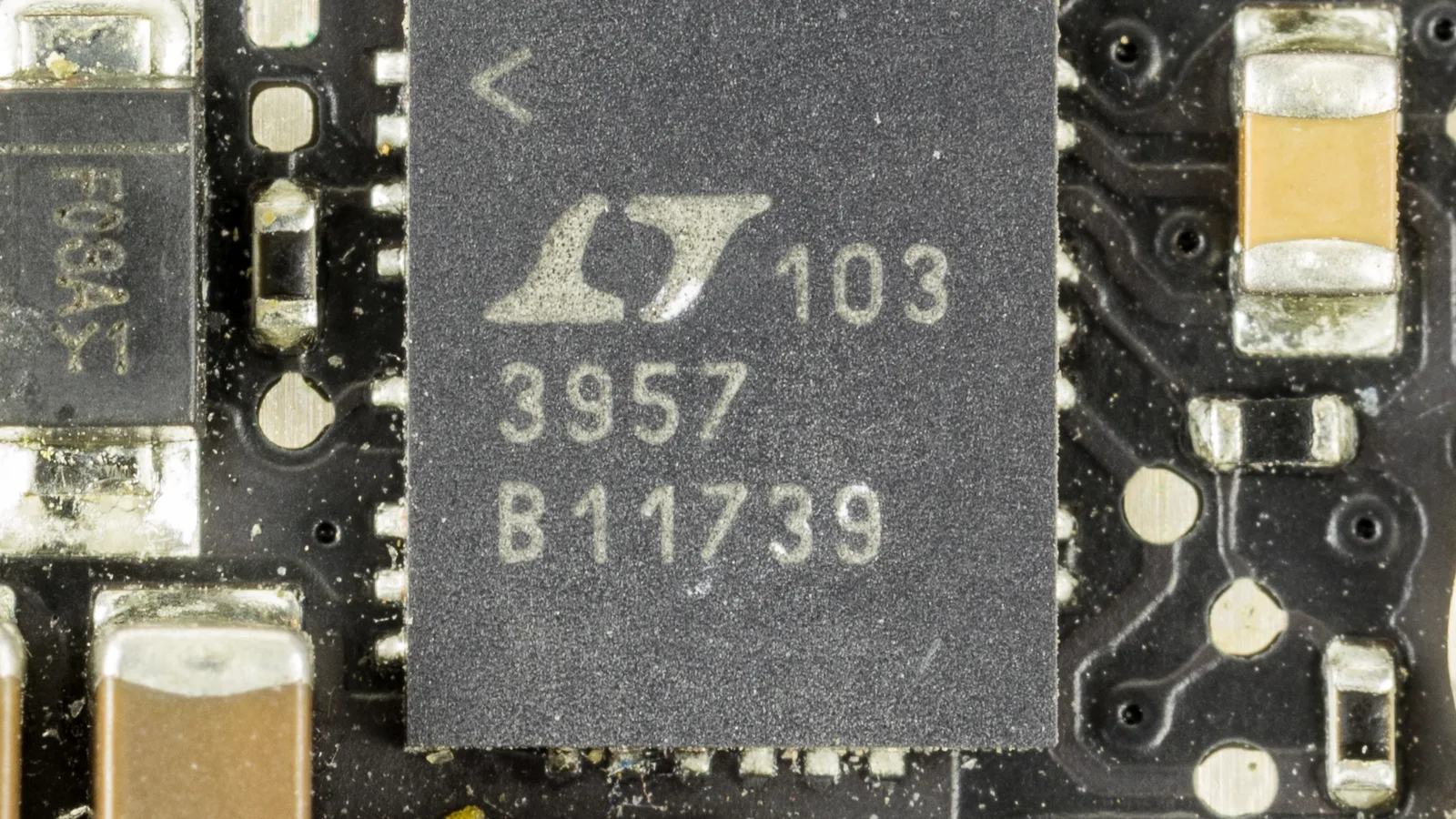 特写：深色电路板上一颗方形黑色小芯片，印有 LT 标志和数字 3957，四周焊着细小的元件