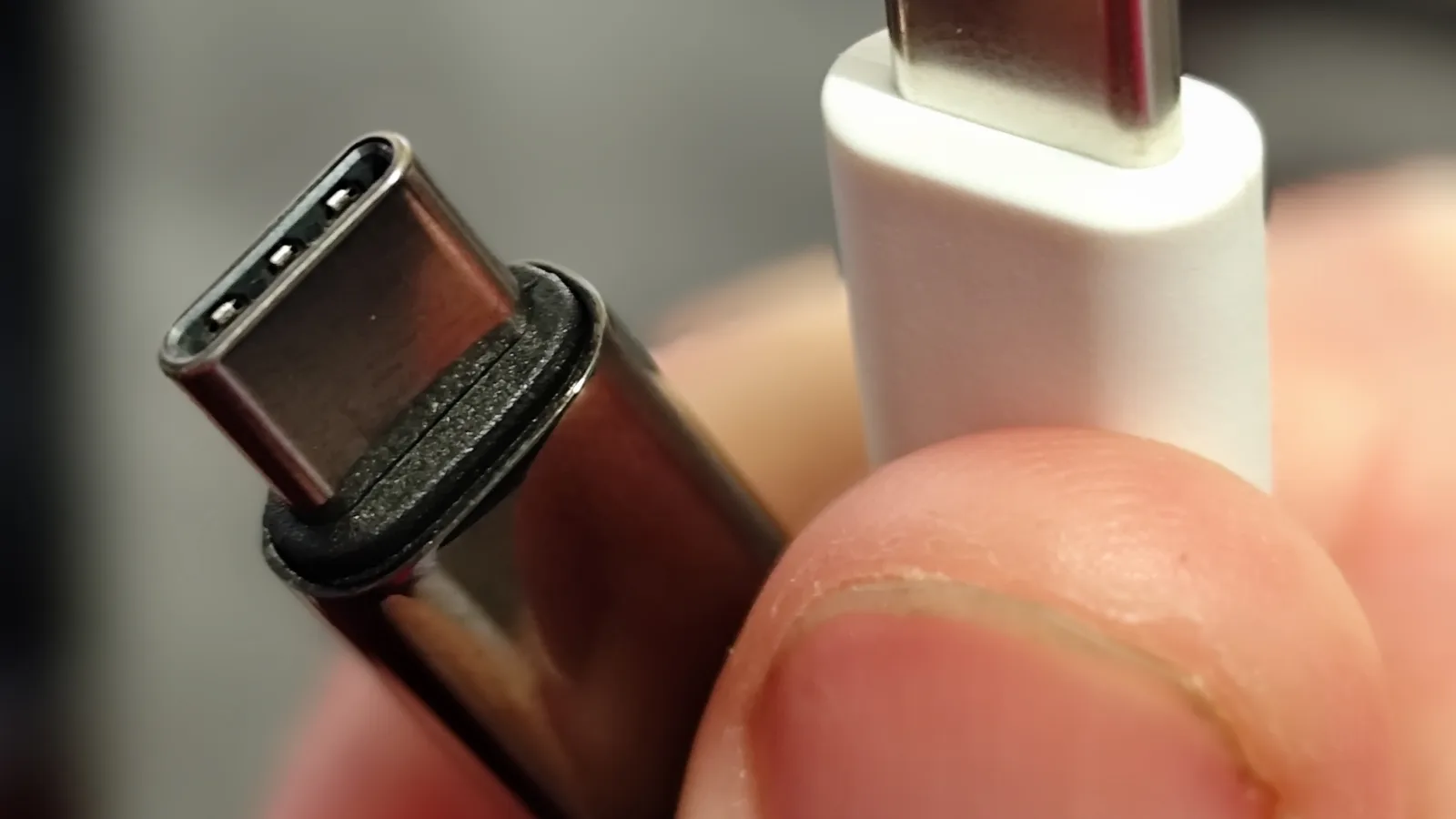 特写下被手指描着的两个 USB-C 数据线接头，一个接黑线、一个接白线。