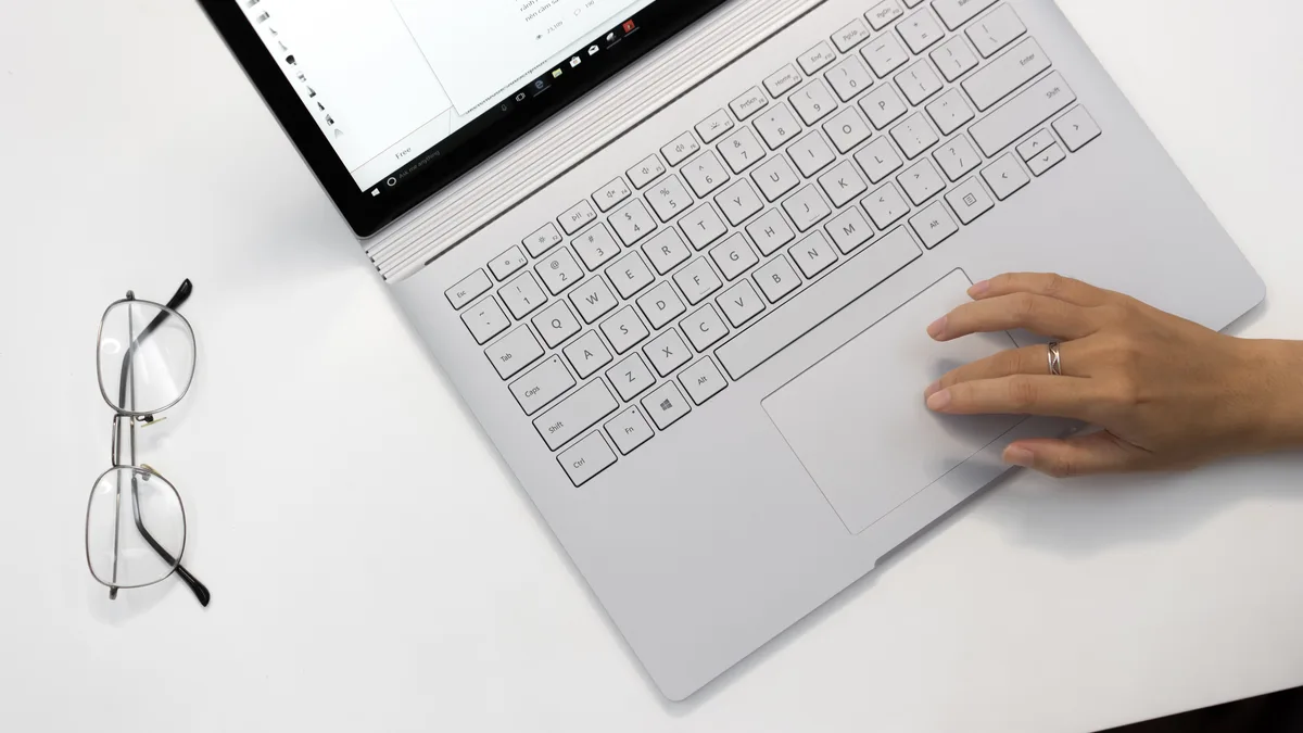 白色桌面上打开的 Microsoft Surface Book 2 俯视图,一只手放在触控板上