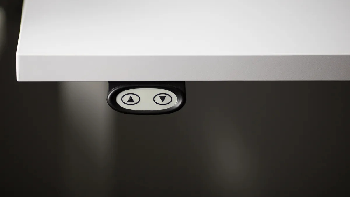A black oval desk controller under a white desktop with only two buttons, up and down, and no memory presets