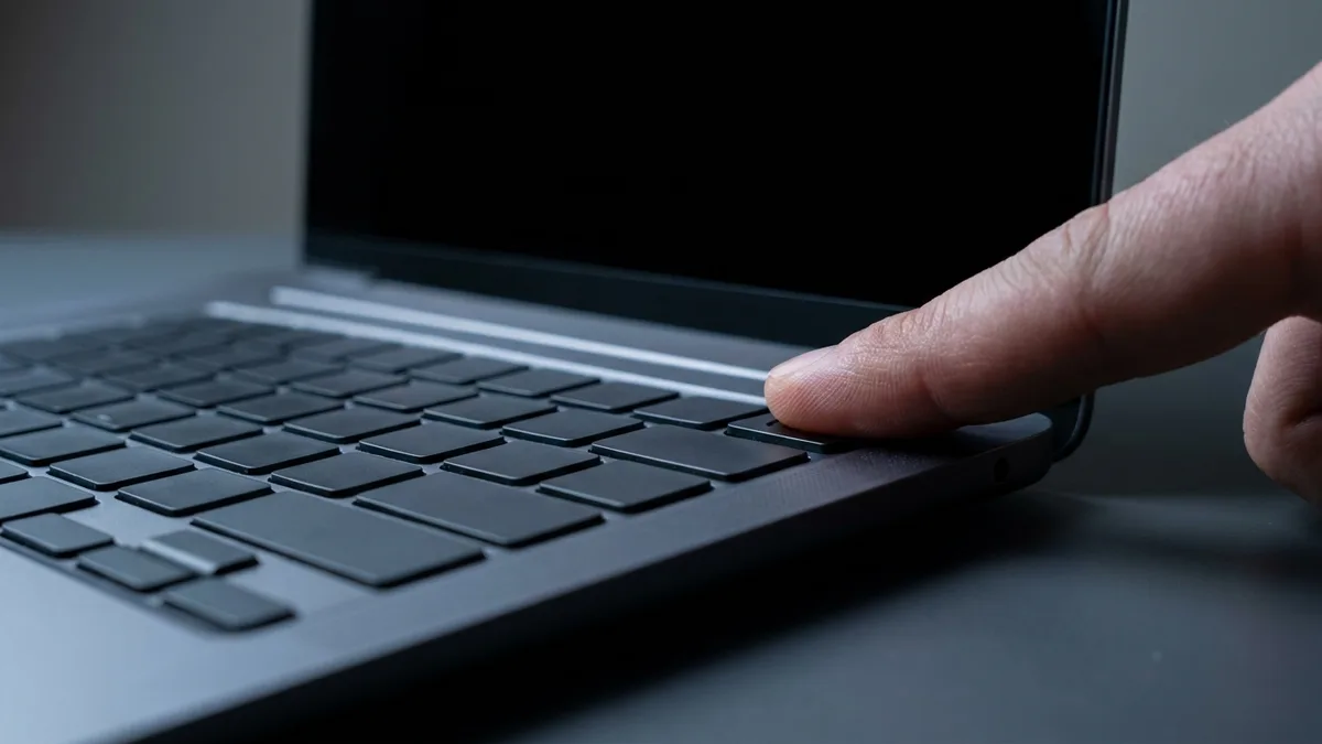 A fingertip pressing and holding a key at the top-right corner of a laptop keyboard, screen dark