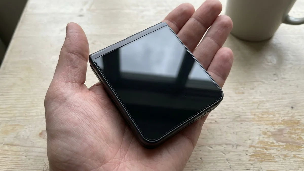 A closed clamshell folding phone lying in an open palm, seen from above to show how small it folds