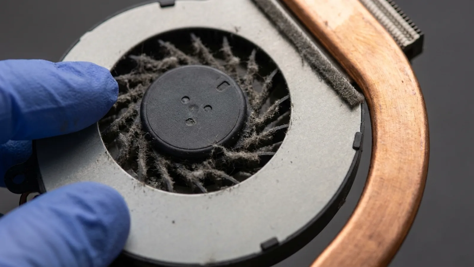 Thick dust clogging the blades of a laptop cooling fan beside its copper heat pipe