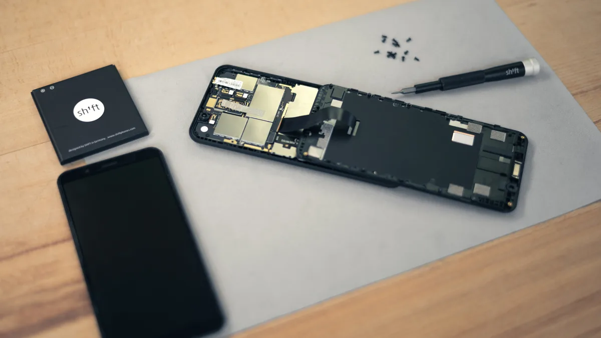 A smartphone opened on a repair mat with its battery removed, screws and a screwdriver laid out