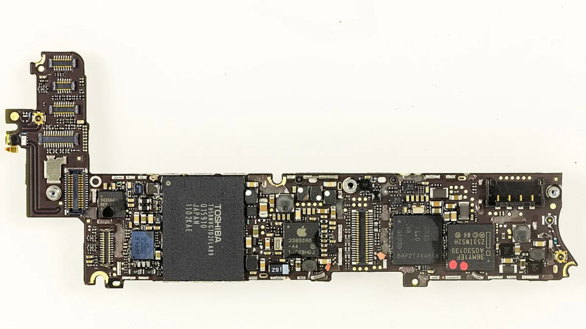 A bare iPhone logic board photographed flat against a white background, its long narrow shape crowded with memory chips, connectors and hundreds of surface-mounted components.