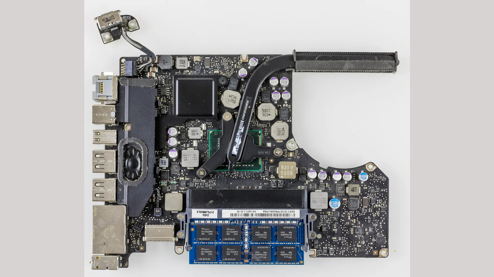 Papan logik Apple MacBook Pro yang dikeluarkan dari kotaknya, dengan cip, memori dan penyambung terdedah serta berlabel.