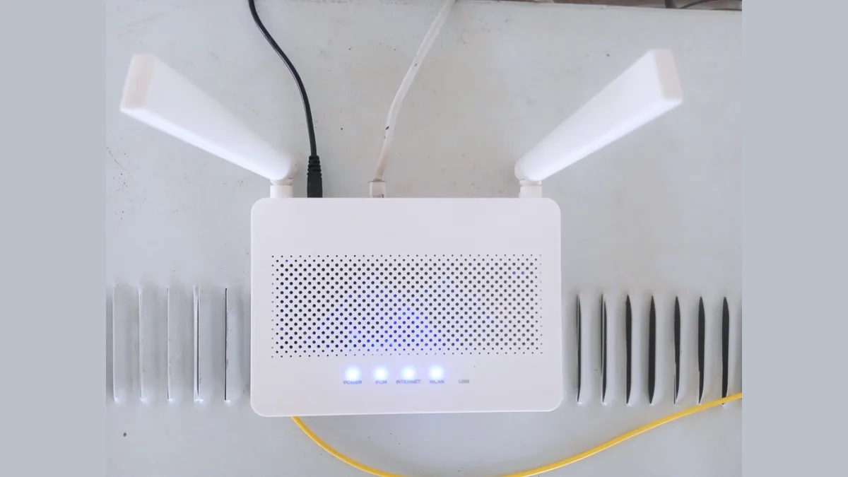 Penghala rumah putih tanpa jenama pada dinding, lampu POWER, PON, INTERNET dan WLAN menyala, dengan kabel fiber kuning bersambung kepadanya